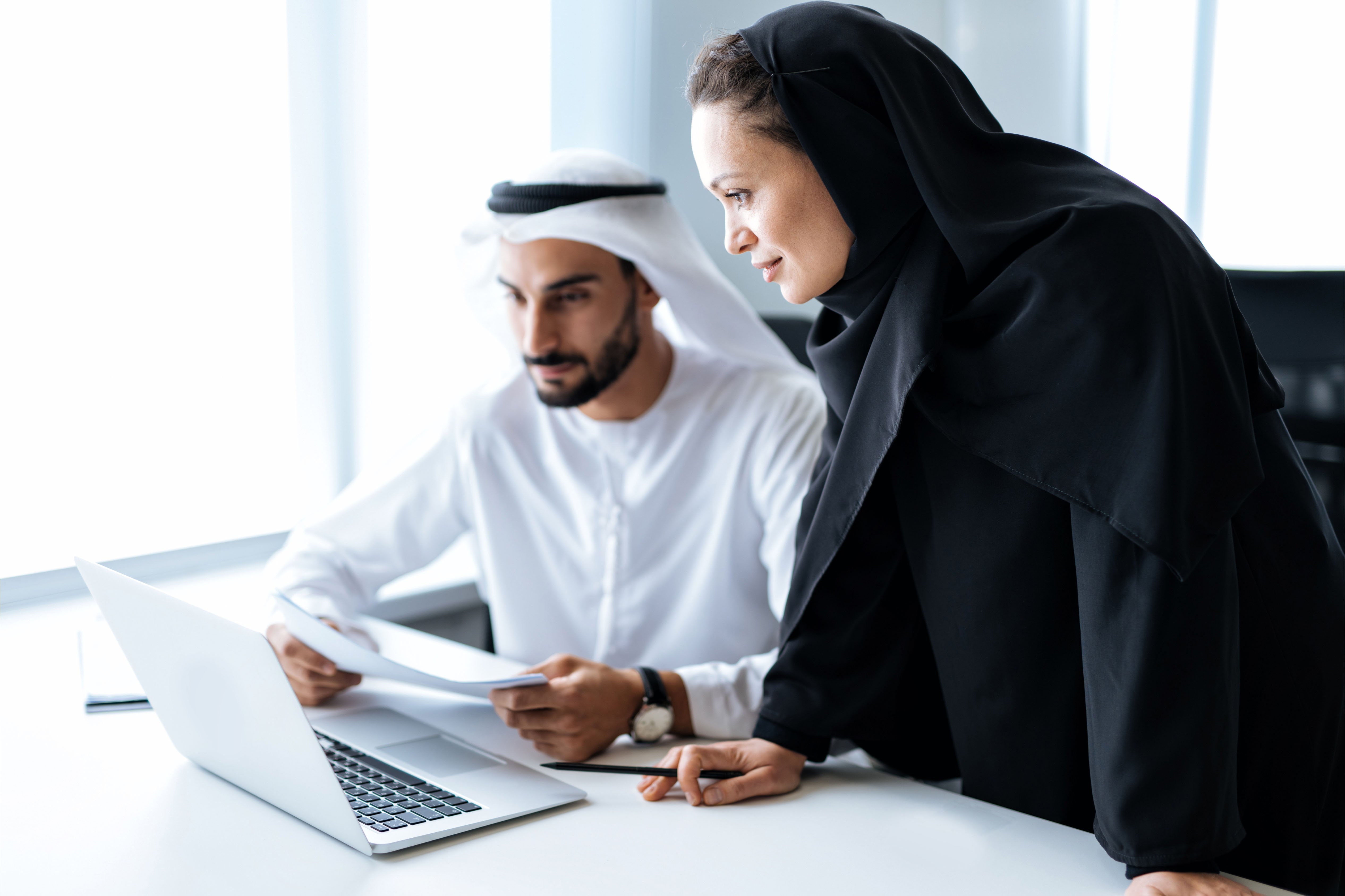 Two Emirati professionals working together on a laptop, analysing documents in a modern office — symbolising data-driven employee benefits insights with Howden Be in the UAE.