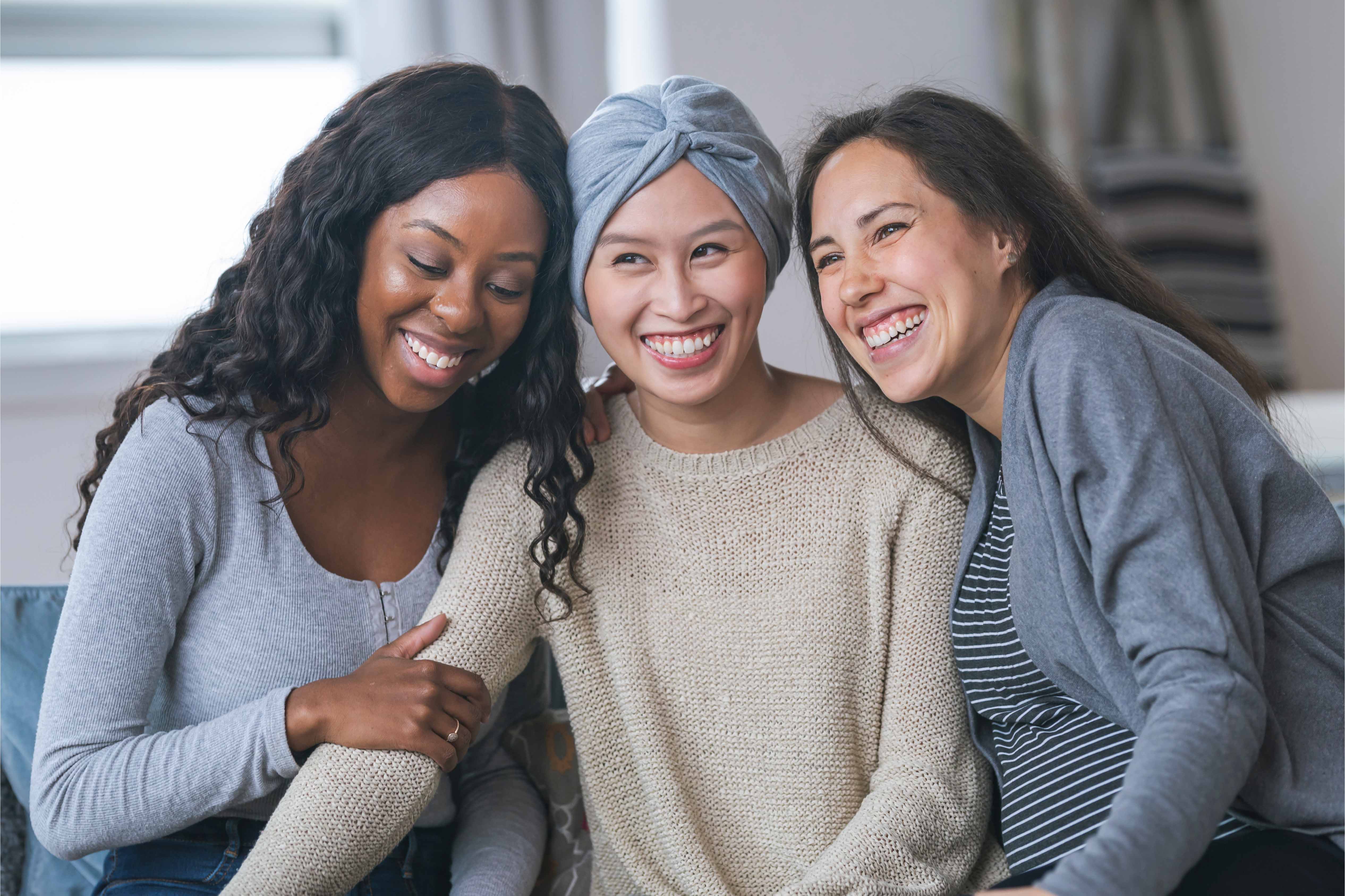 Three women smiling and embracing, symbolising support, resilience, and the importance of critical illness cover and wellbeing benefits for employees in the UAE.