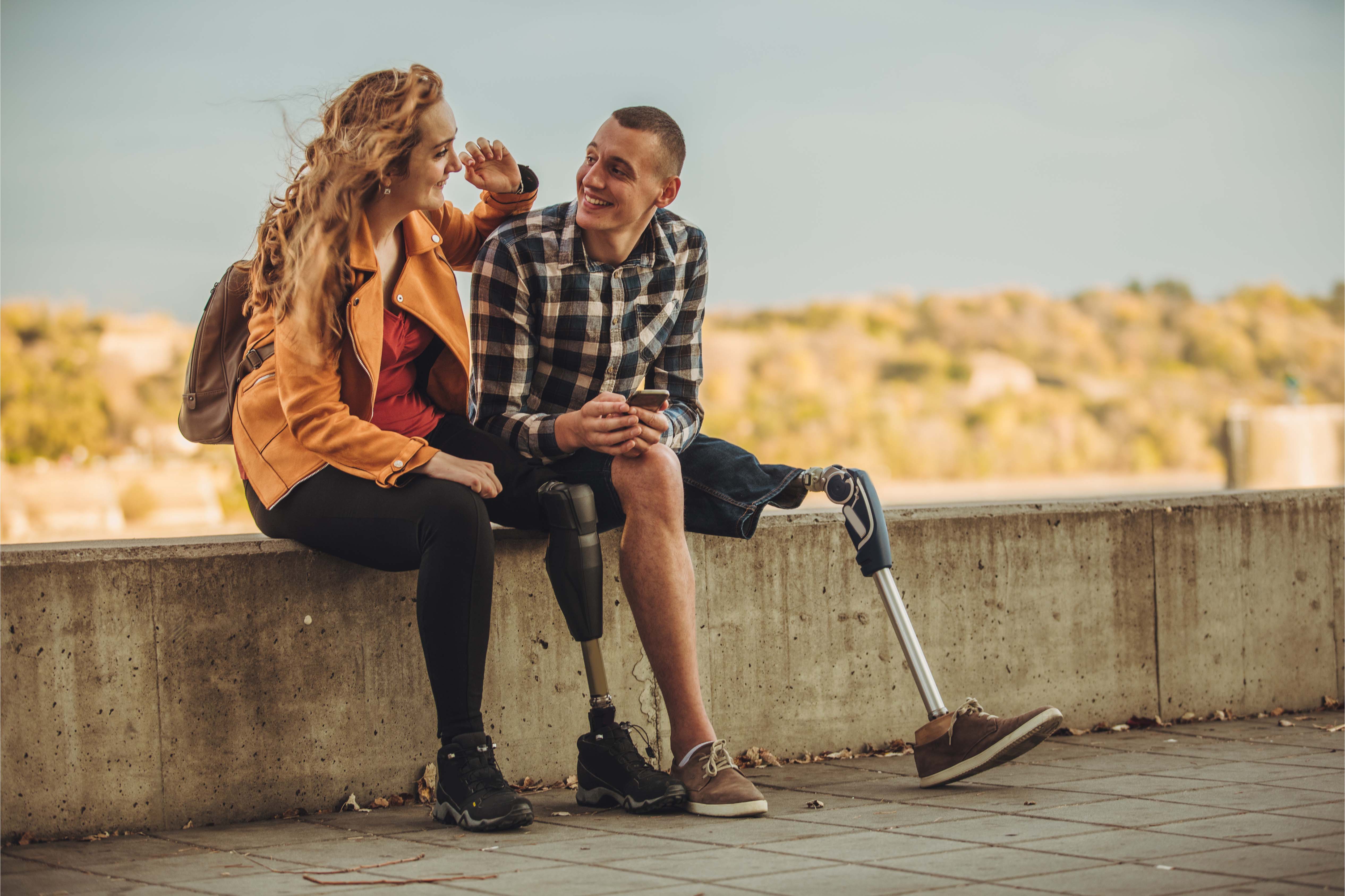 A young man with a prosthetic leg sitting outdoors with a friend, smiling and relaxed — symbolising resilience, inclusion, and the value of income protection and group risk benefits in the UAE.