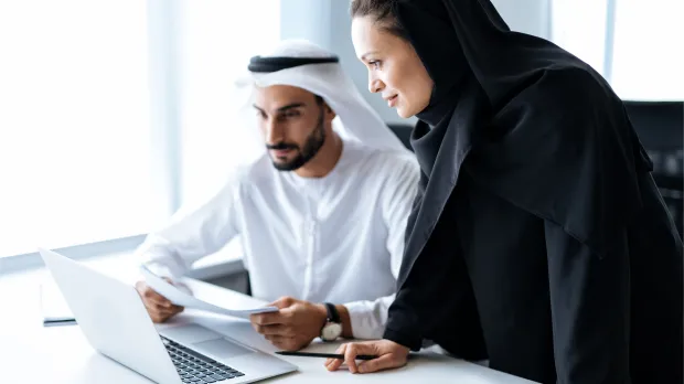 Emirati professionals reviewing data on a laptop in UAE office Two Emirati professionals working together on a laptop, analysing documents in a modern office — symbolising data-driven employee benefits insights with Howden Be in the UAE.