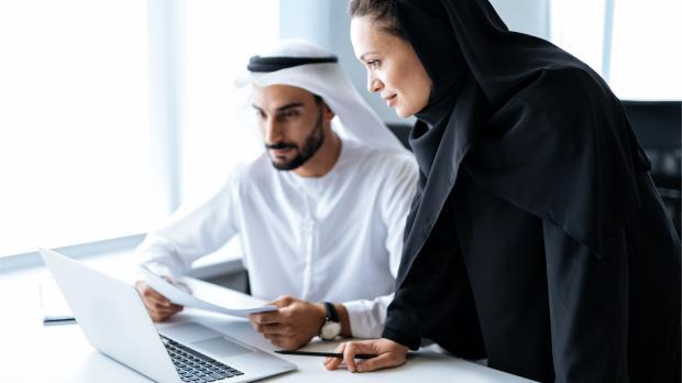 Two Emirati professionals working together on a laptop, analysing documents in a modern office — symbolising data-driven employee benefits insights with Howden Be in the UAE.