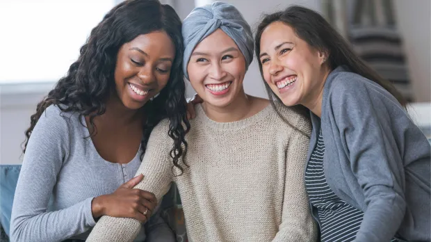 Friends supporting each other with care and positivity Three women smiling and embracing, symbolising support, resilience, and the importance of critical illness cover and wellbeing benefits for employees in the UAE.