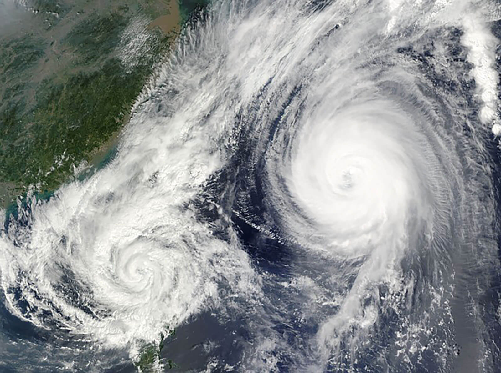 Satellite view of hurricanes over ocean near coastline, powerful tropical cyclones with visible storm eye, extreme weather system, and natural disaster monitoring from space.