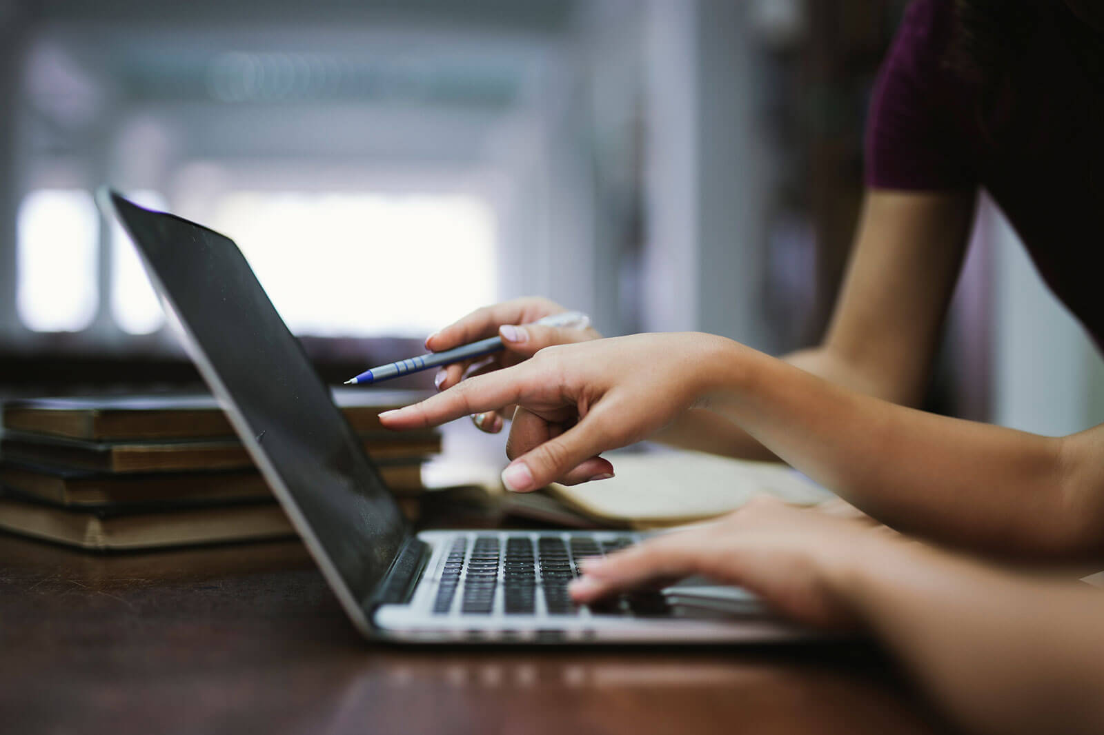Close-up of hands using laptop computer for online work, digital collaboration, remote learning, or business communication in modern workspace.