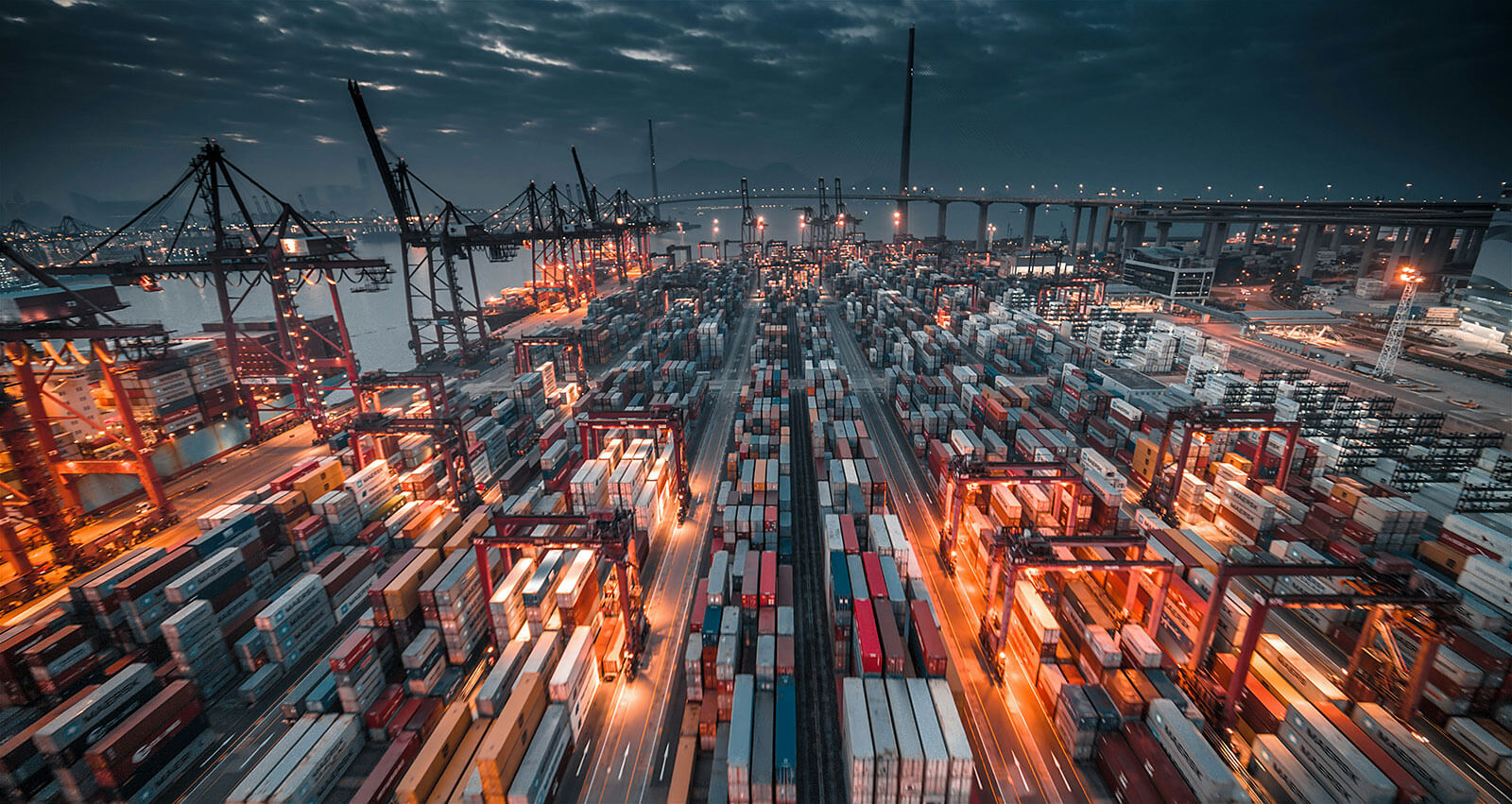 Busy container shipping port at night with stacked cargo containers, cranes, and logistics operations, showcasing global trade, freight transportation, and maritime supply chain infrastructure.