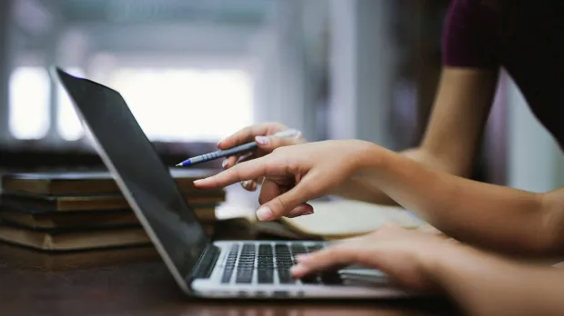 Close-up of hands using laptop computer for online work, digital collaboration, remote learning, or business communication in modern workspace.